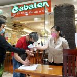 Resto shift manager Janine Alunday (right) uses a thermal gun to check the temperature of a customer before entering the establishment inside the mall on Quirino Highway, Fairview, Quezon City on Wednesday (Oct. 20, 2021). Indoor dine-in services in restaurants are allowed by Inter-Agency Task Force for the Management of Infectious Diseases (IATF) for a 30-percent venue capacity except for those areas under granular lockdown. (PNA photo by Ben Briones)
